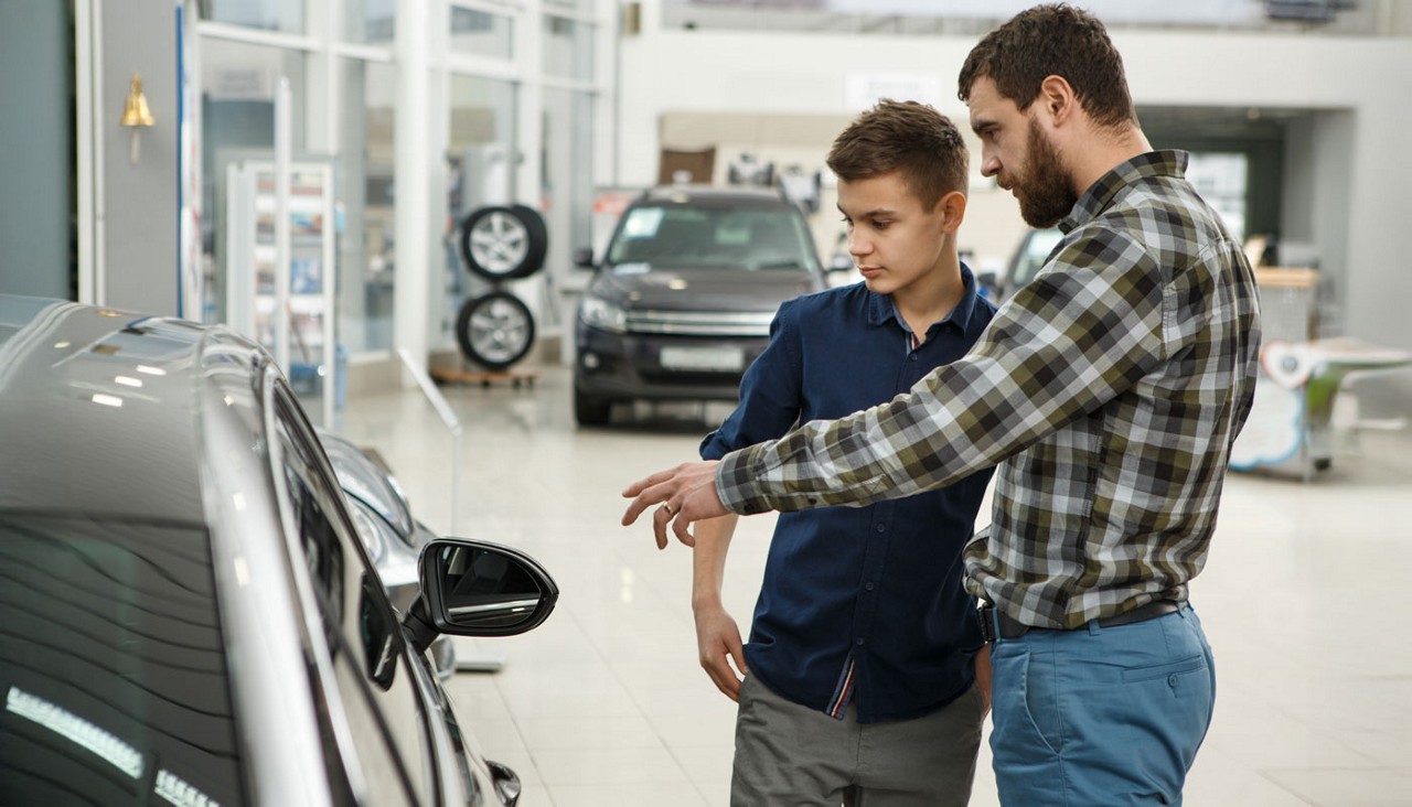 A father with his son looking at new cars in a dealership showroom.
