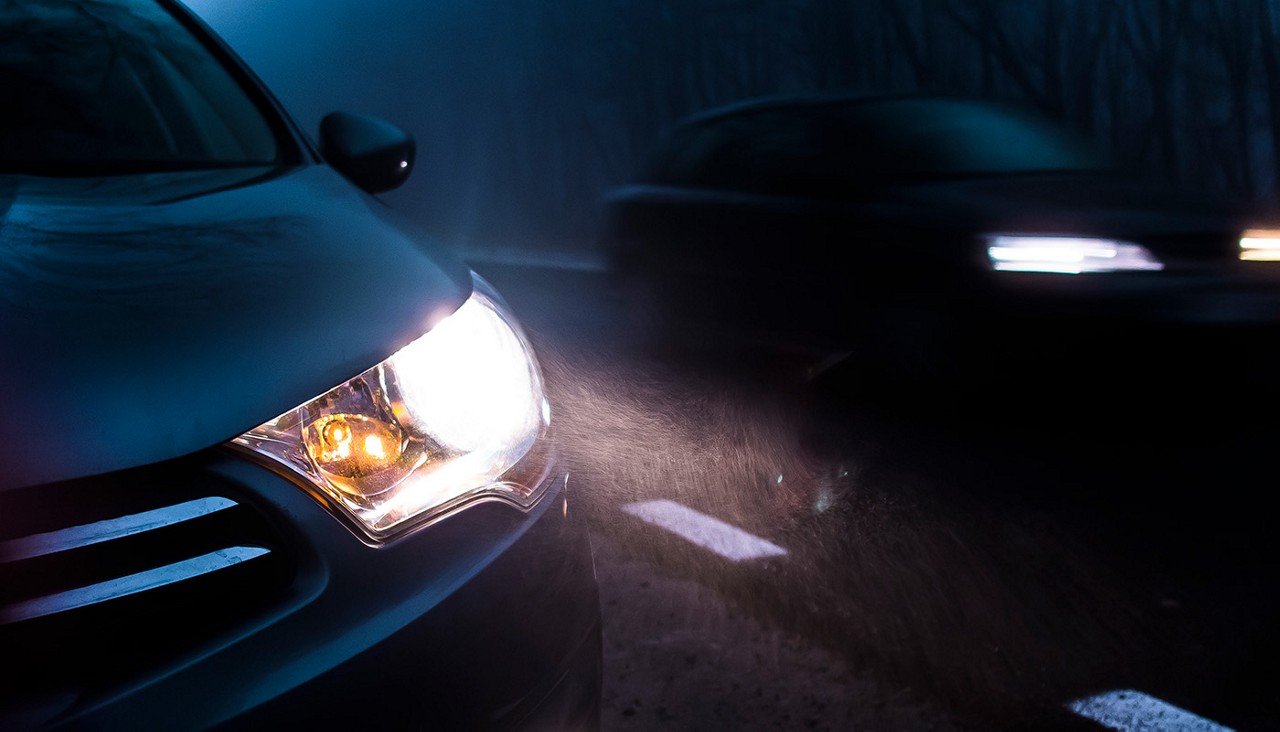 A close-up view of a car's headlights shining through a dark foggy night.