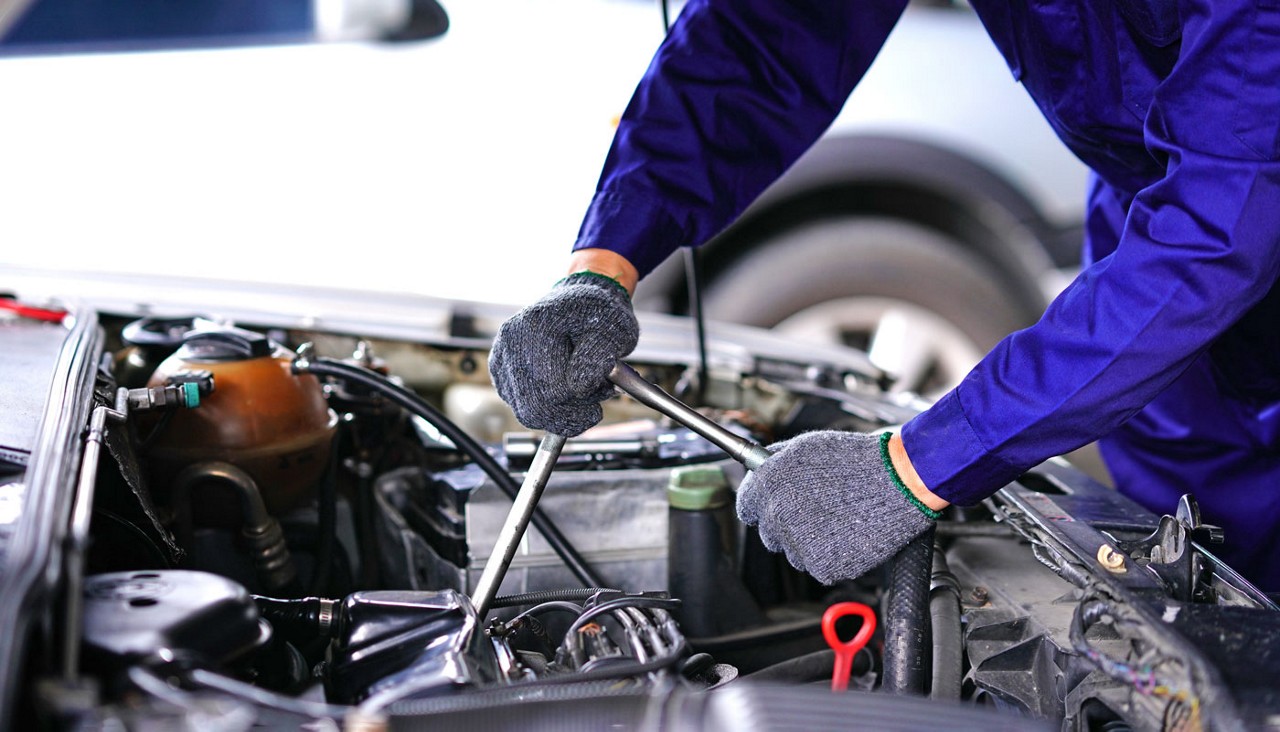 A close-up view of a mechanic working under the hood of a vehicle.