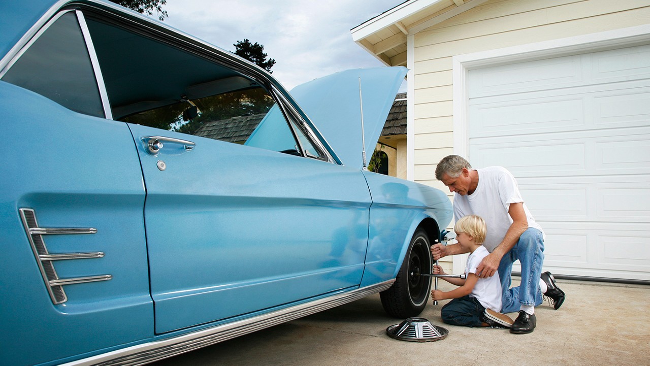 A father showing his son how to change the tire on a vintage light blue Ford Mustang