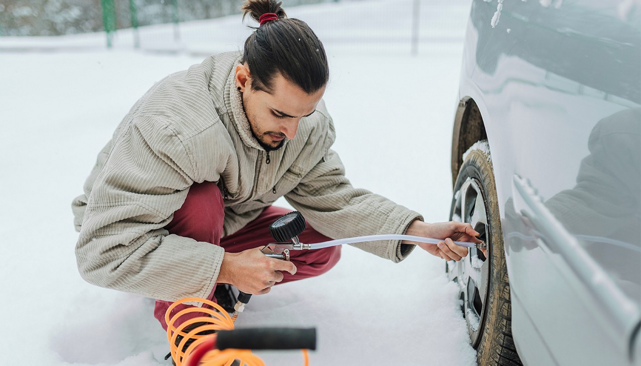 A man checking his tire's pressure while it is stuck in a snowbank in cold weather.