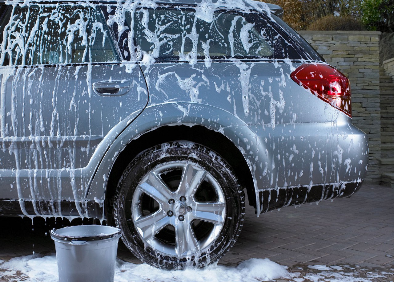 A station wagon vehicle being washed. A bucket and lots of soap suds are visible.
