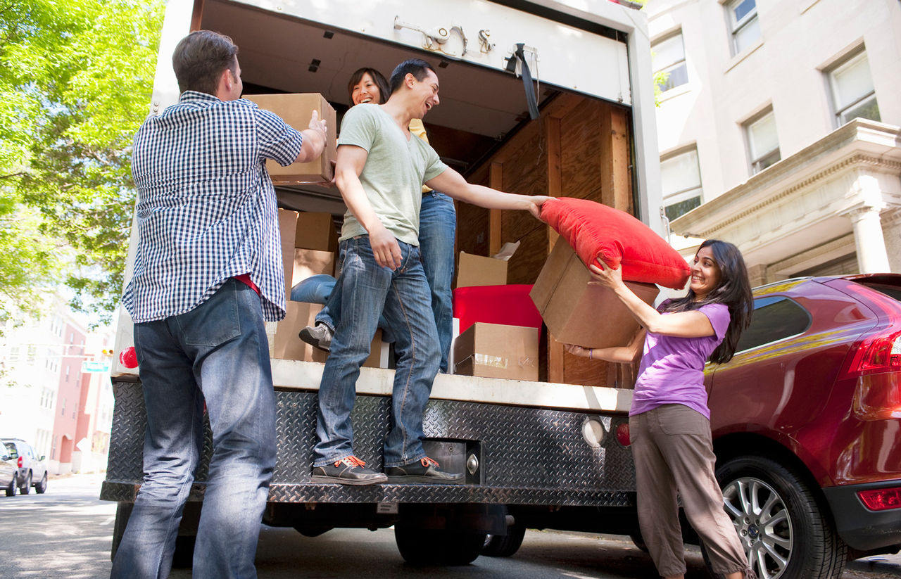 adult friends moving boxes from back of moving truck