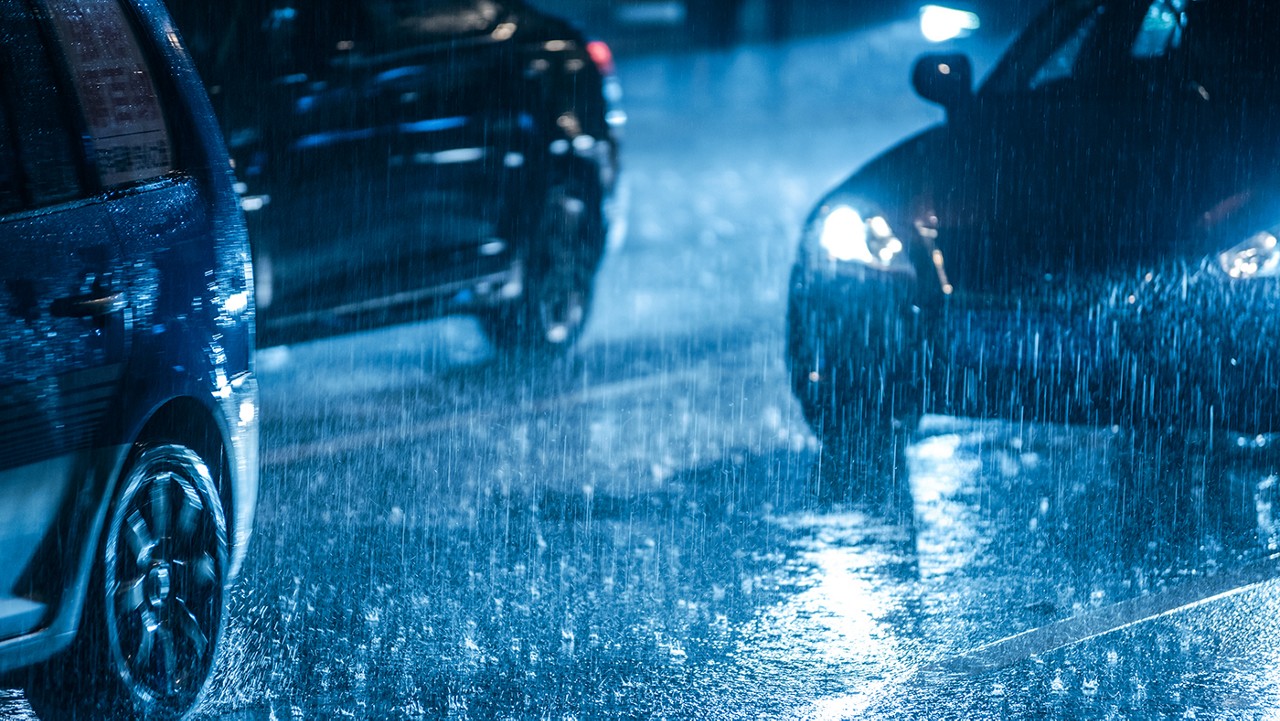 A dark rainy night with several cars driving closely on a highway.