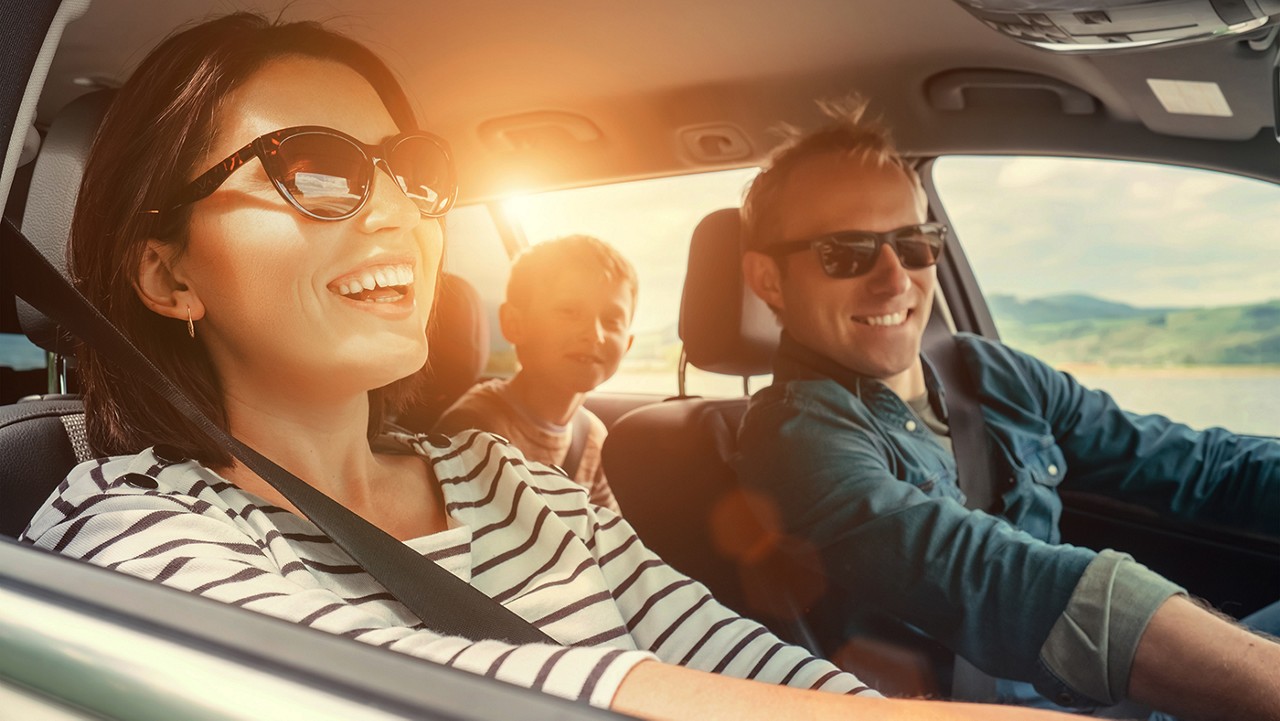 A family riding in a car with sunglasses on and the sun glaring in their faces.