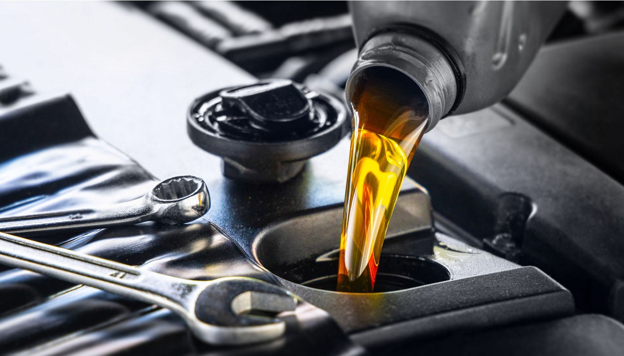 Close-up view of a bottle of engine oil being poured into the engine valve for oil.