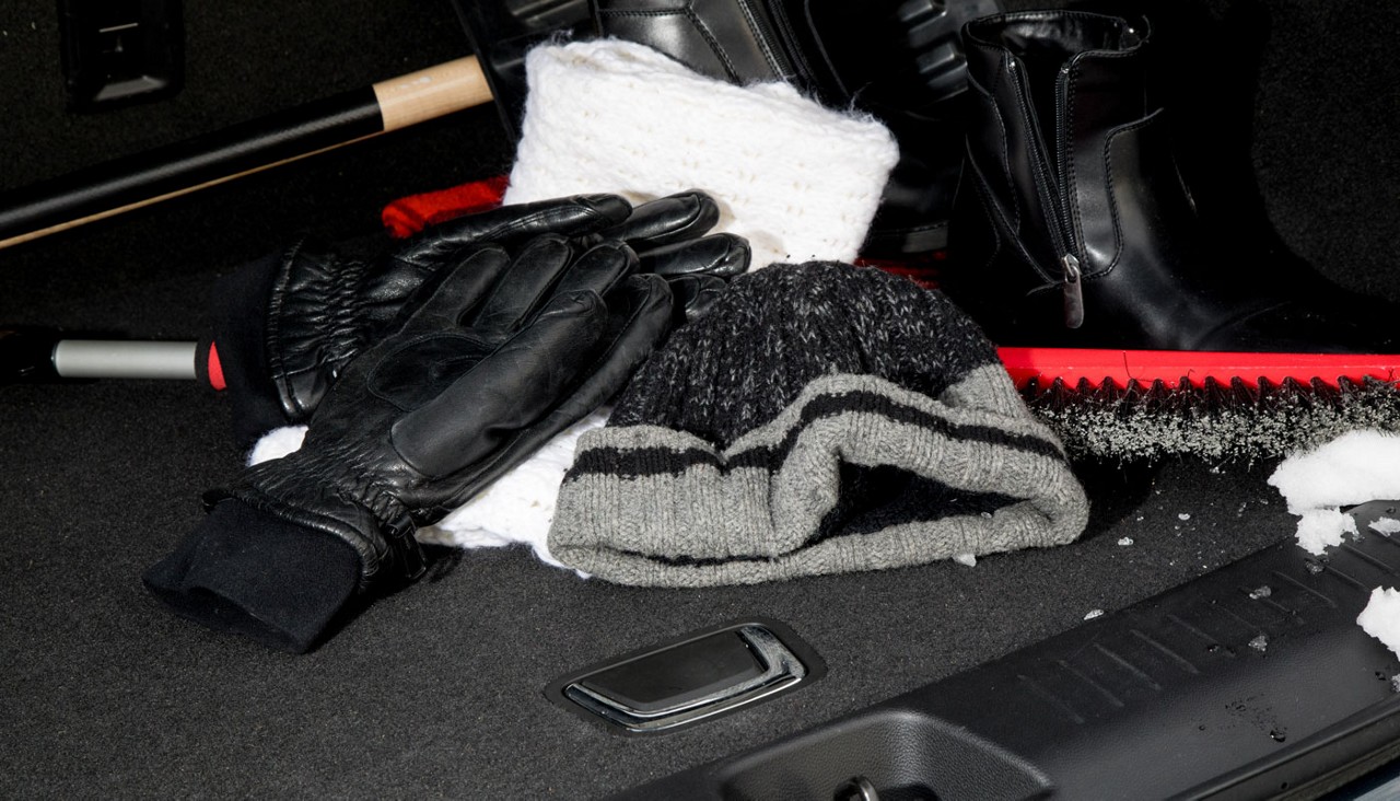 A pair of winter gloves, a stocking cap, a snow brush and other equipment in a trunk.