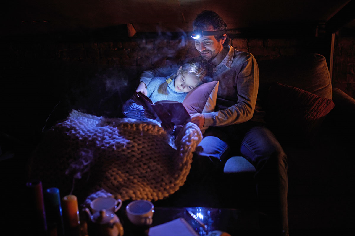 A father with a headlamp on reading a book to his daughter at night.