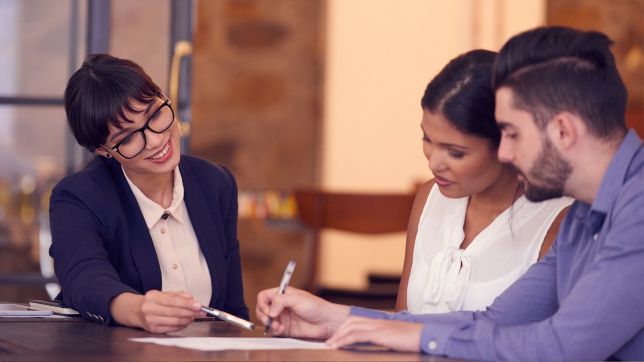 A young couple reviewing paperwork with a woman in a business suit.