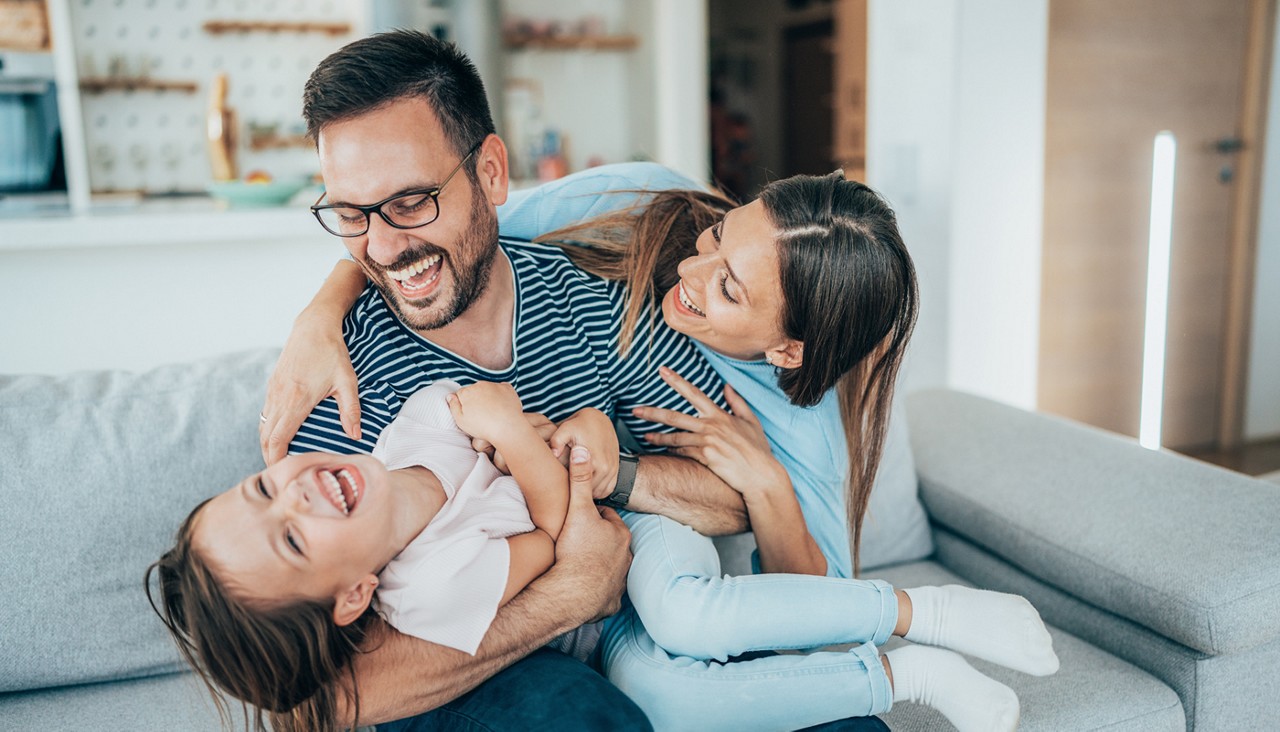 A father and two daughters playing games on the couch.