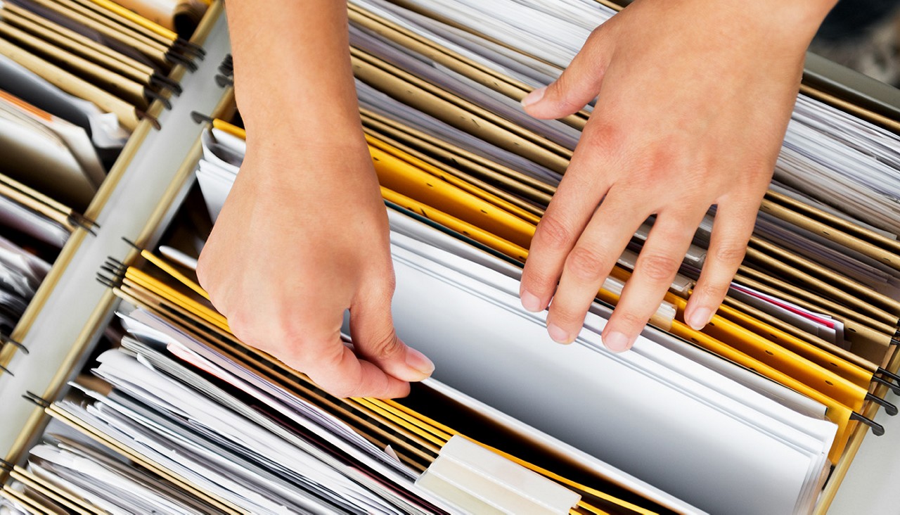 Close-up view of a person's hands as they look through files in a filing cabinet