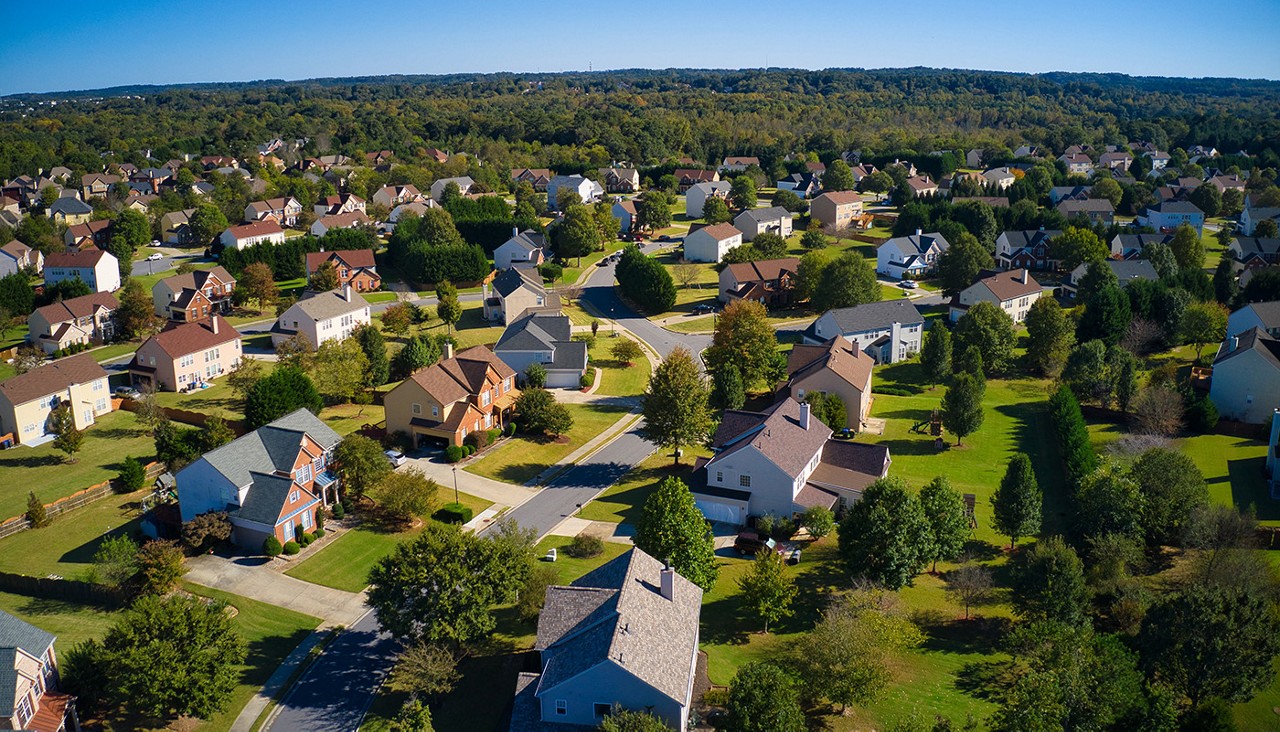 An aerial view of a suburban neighborhood with hundreds of rooftops visible.