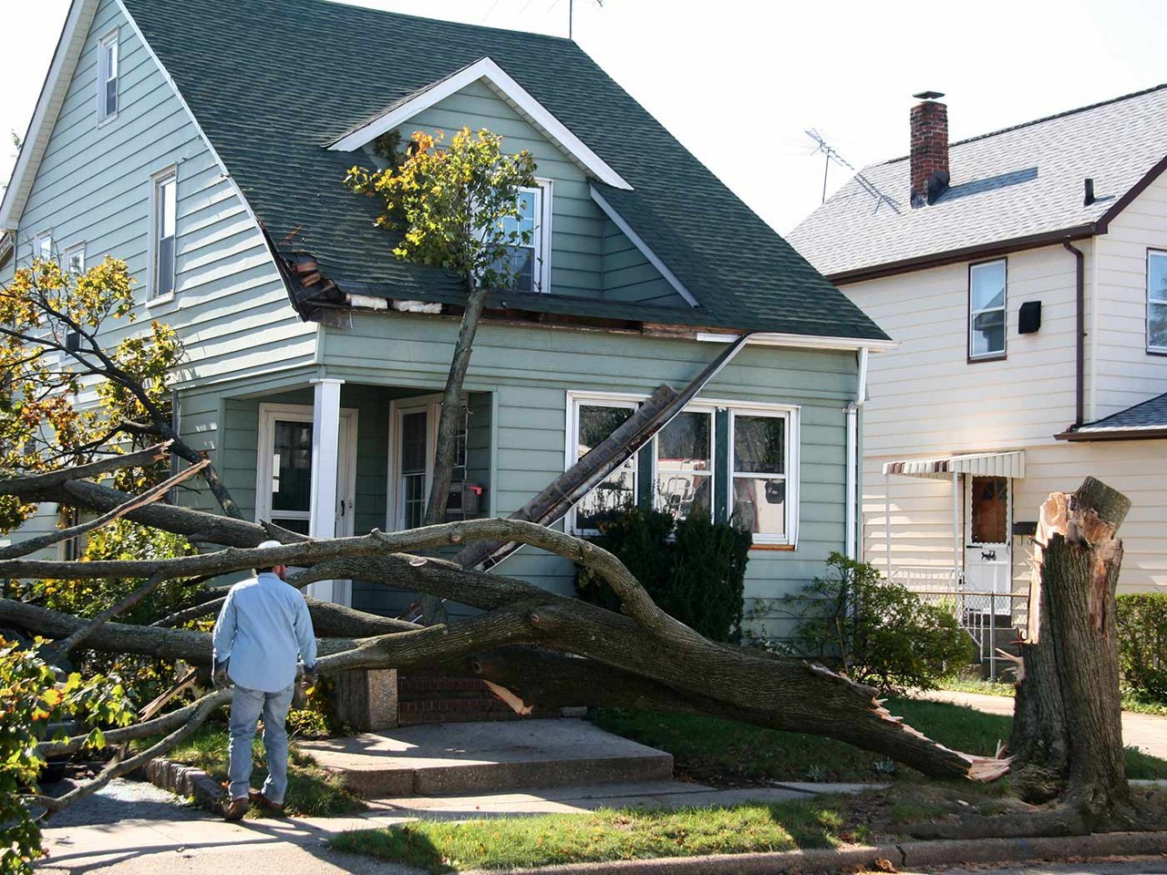 The front of a house that has had a tree fall on it and the sidewalk