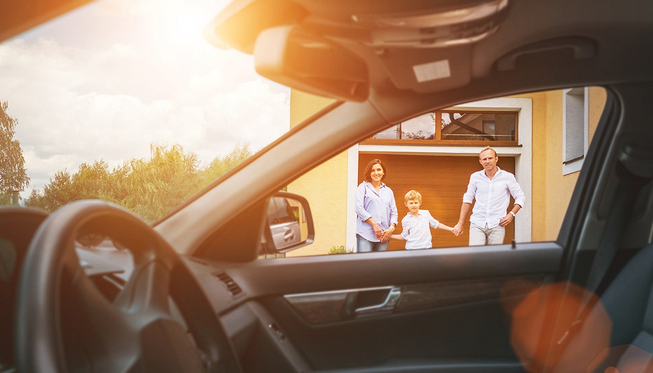 A family of three in the doorway of their home looking out toward a car.