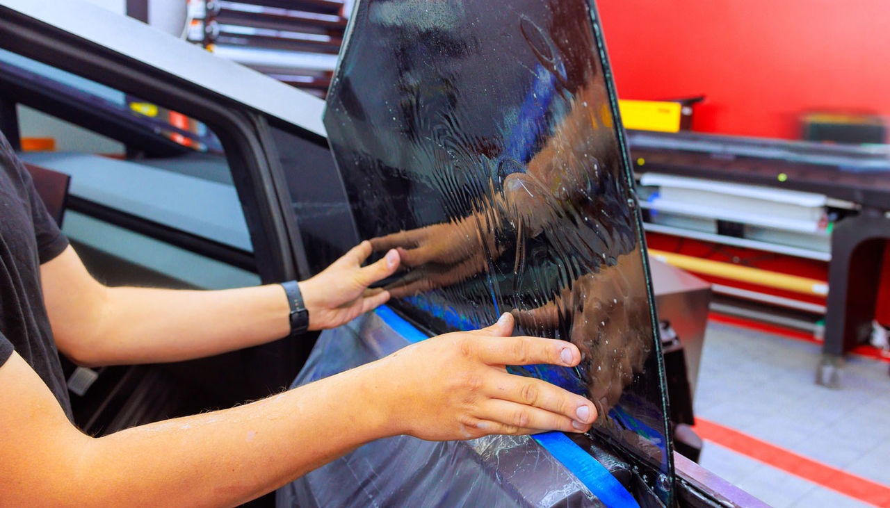 Technician worker applies tint film to car window in well lit automotive workspace, ensuring perfect fit
