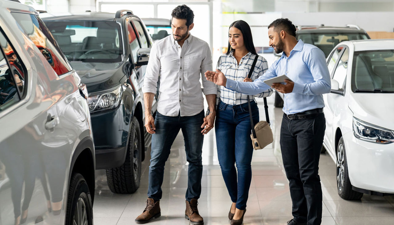 Salesman at the dealership showing a car to a couple