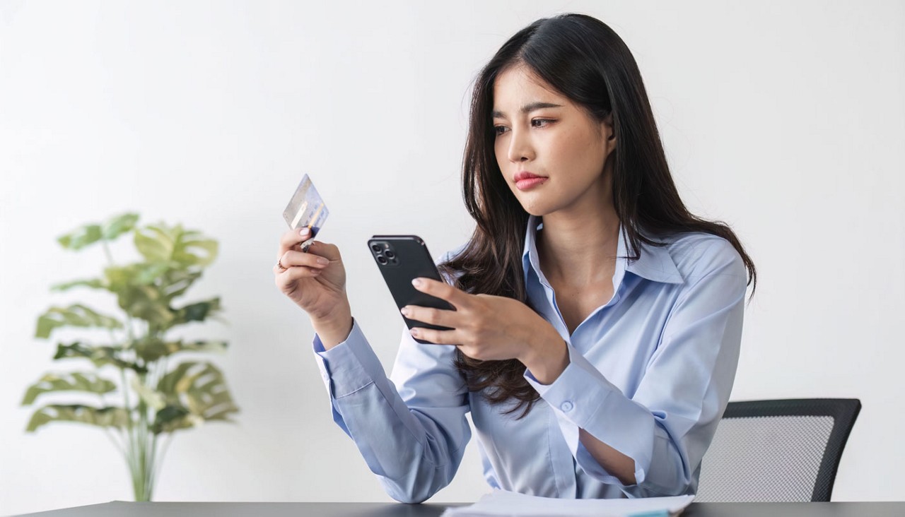 Unhappy young woman at home holding up cellphone and credit card