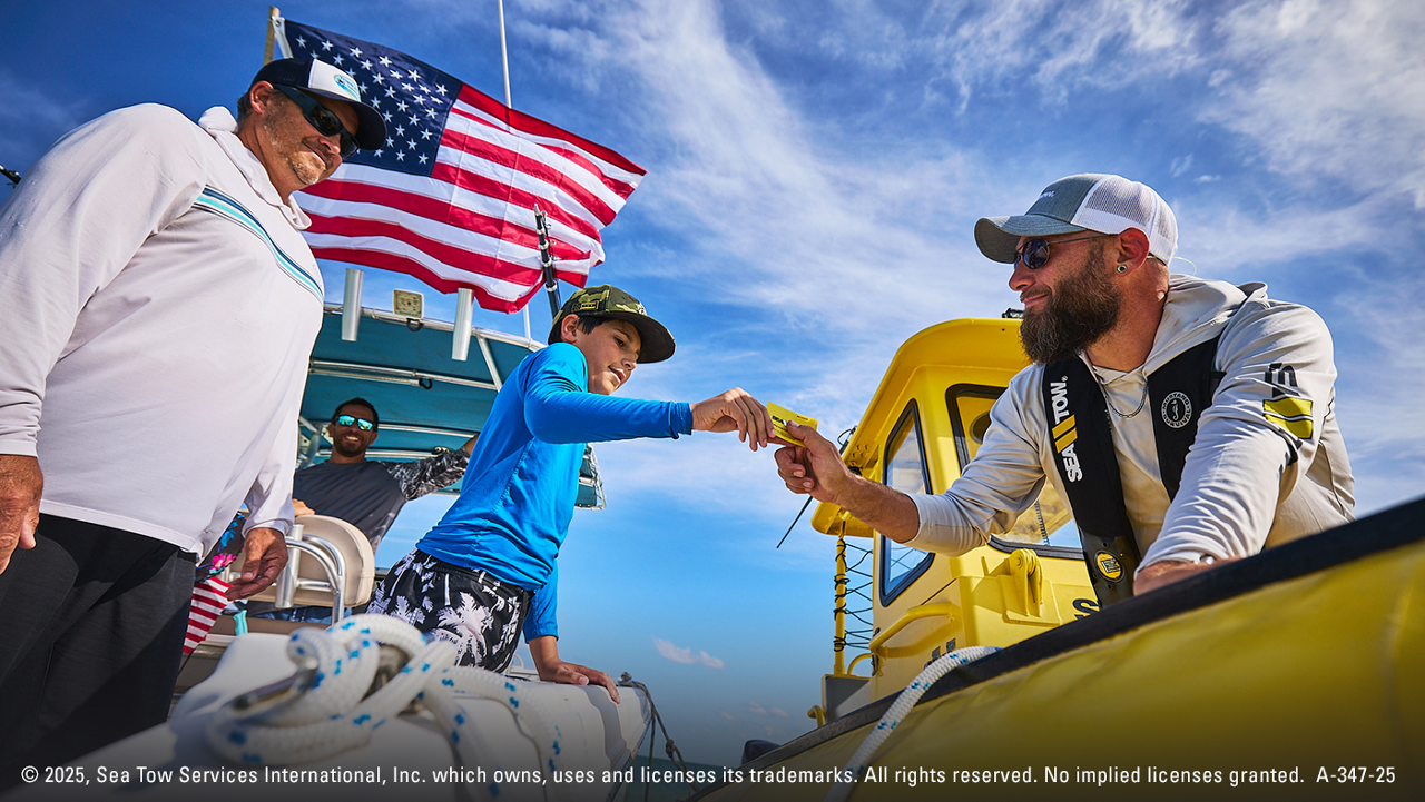 A Sea Tow employee in a yellow boat helping a dad and son with their boat out on the water.