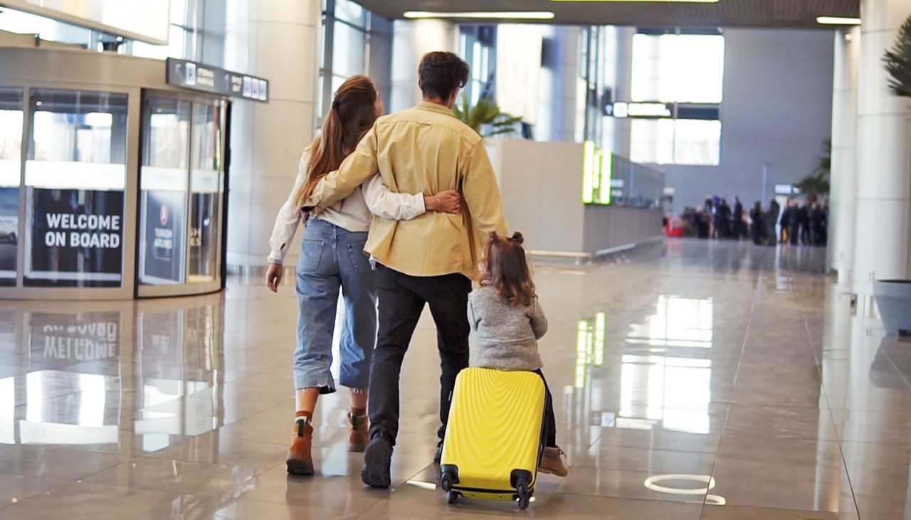 Family of 3 walking through airport with daughter riding on luggage