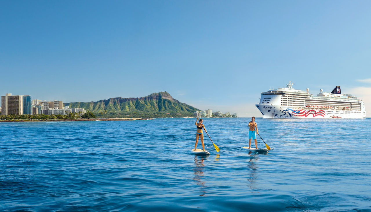Two paddle boarders off the island of Oahu with a cruise ship behind them.